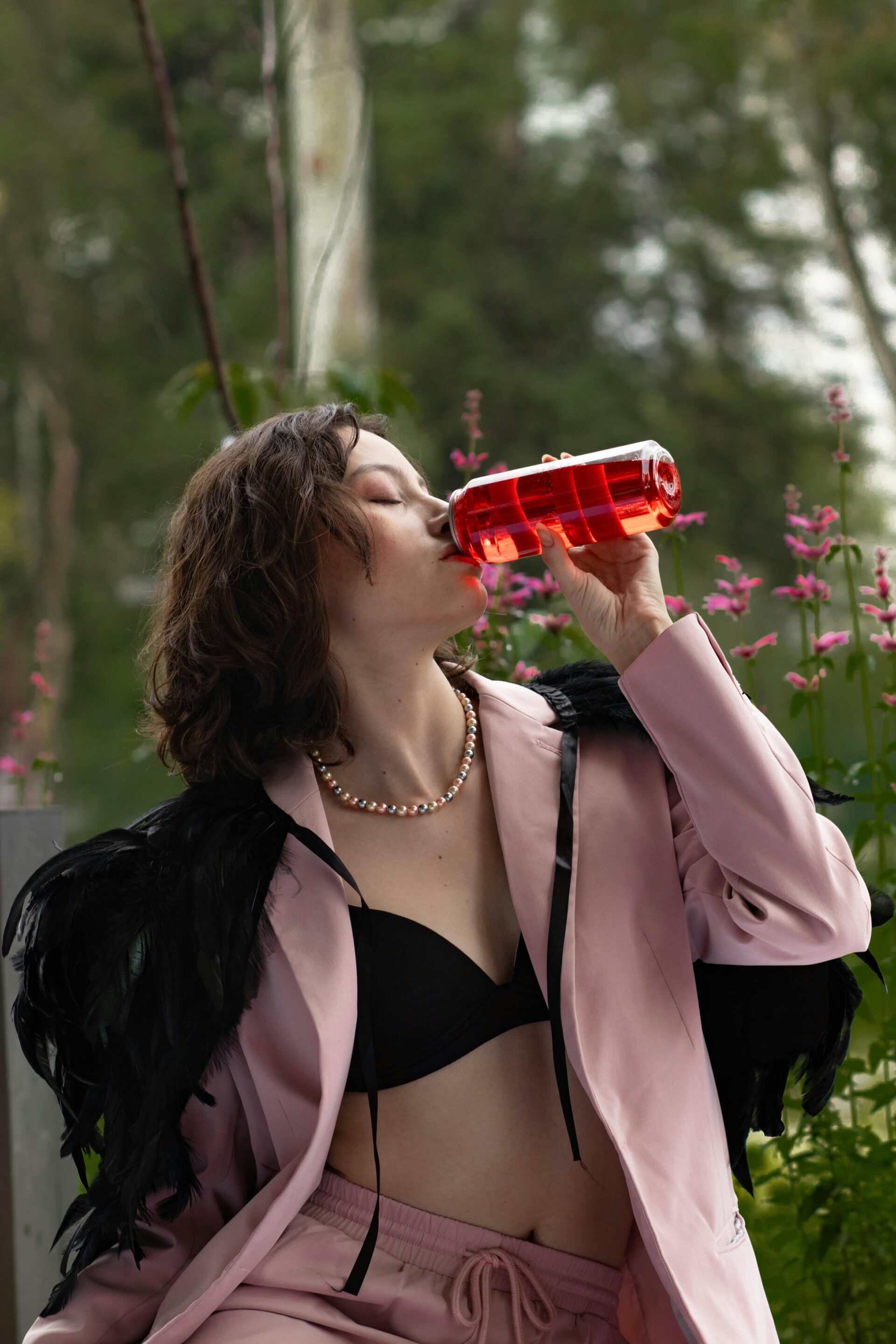 woman-in-stylish-outfit-drinking-from-red-bottle-outdoors