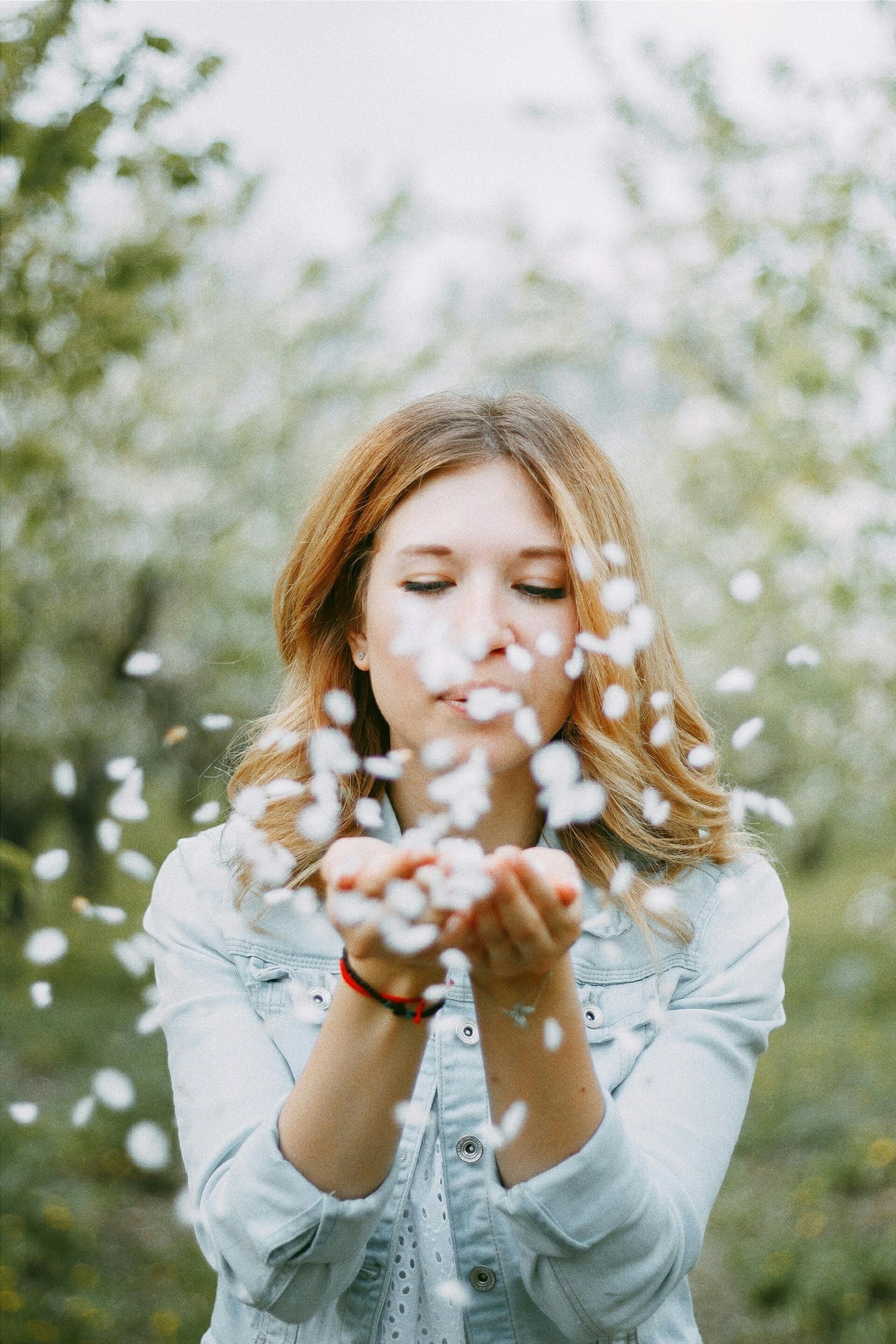 woman-blowing-white-petals-in-orchard