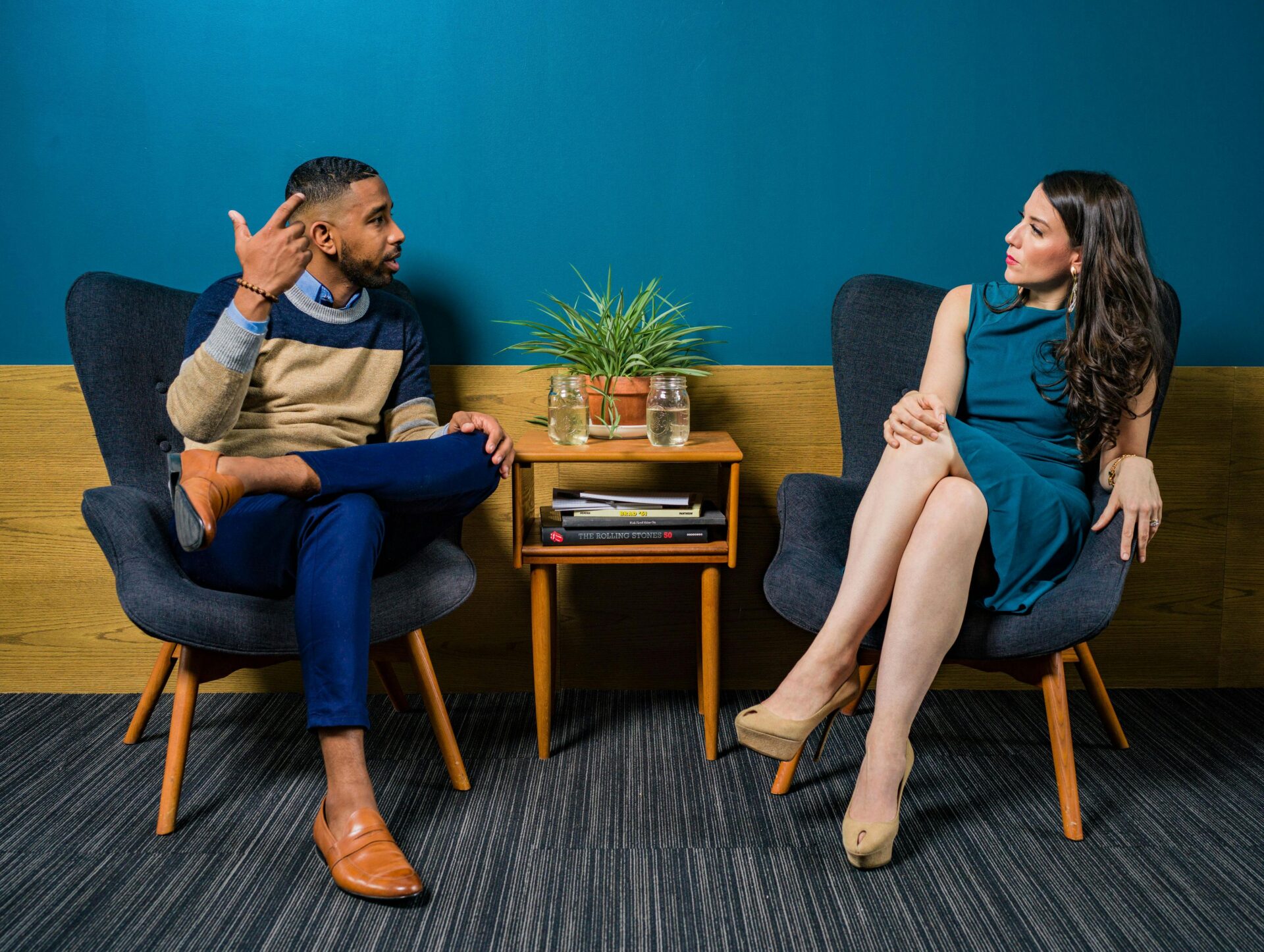 woman-wearing-teal-dress-sitting-on-chair-talking-to-man